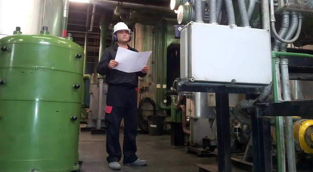 Operario industrial con casco y planos revisando controles de calidad